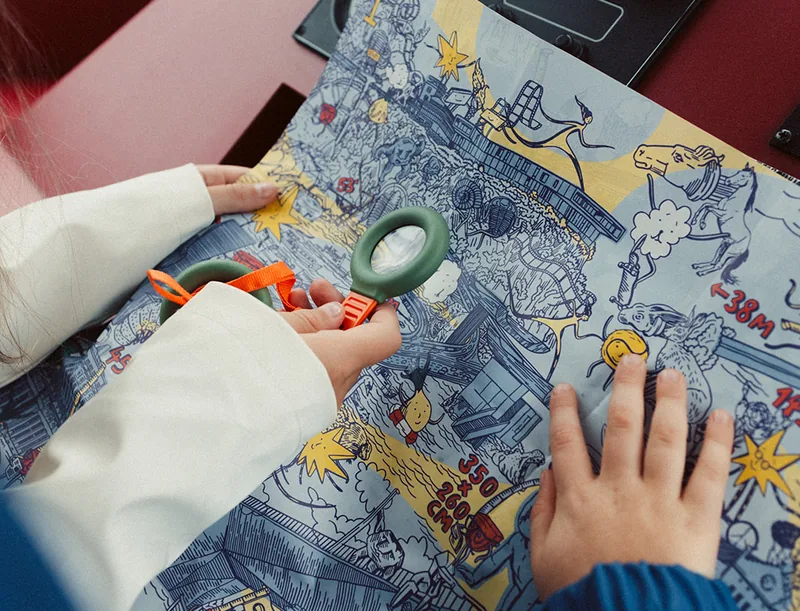 Děti hledají s lupou na rozložené mapě u kormidla lodi